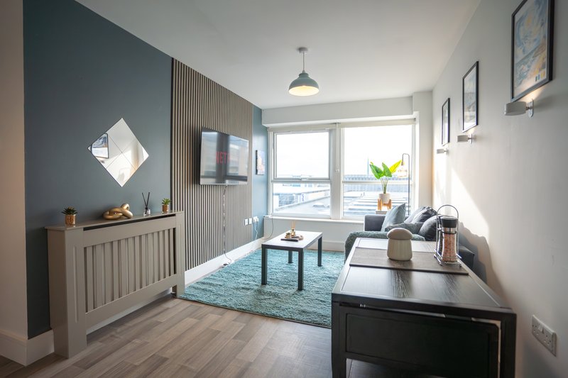 Modern living room with teal accent wall, wooden furniture, desk, and large windows with water view