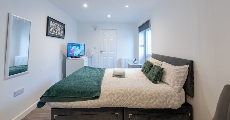 Bright bedroom with double bed, green bedding, small TV, and white door