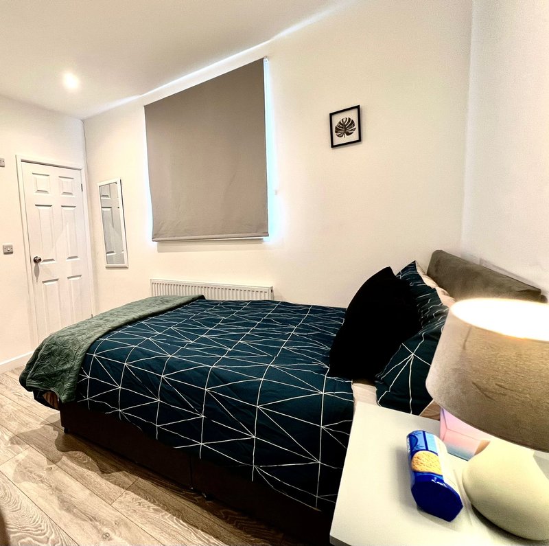 Bedroom with double bed, geometric patterned duvet, nightstand with lamp and toiletries