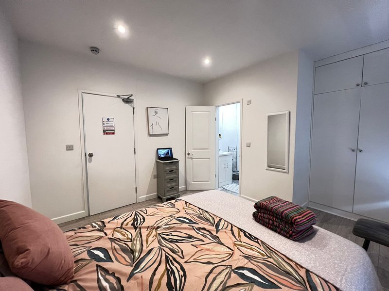 Bedroom with bed, patterned duvet, burgundy cushion, and fitted wardrobes
