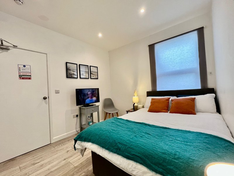 Bedroom with double bed, teal blanket, TV, window and modern furnishings