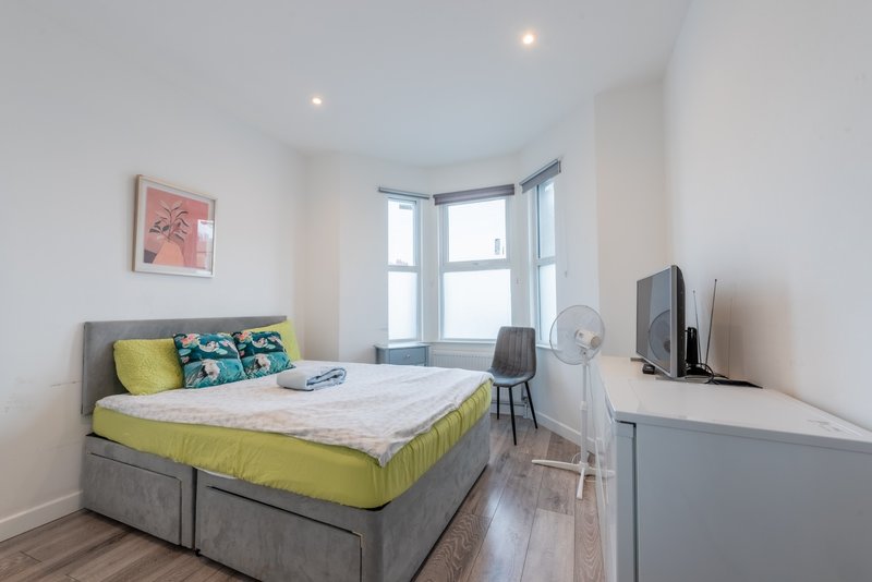 Bright bedroom with double bed, yellow bedding, colorful cushions, desk area and bay window