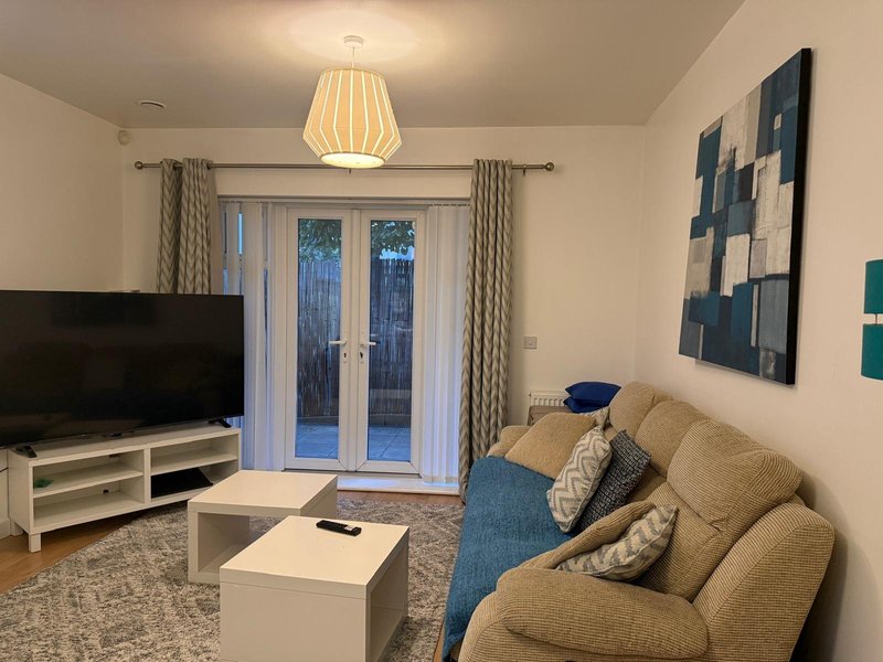 Modern living room with cream sofa, TV, pendant lamp, and glass doors to garden