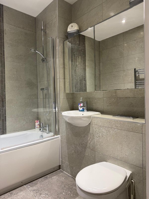 Modern bathroom with grey tile walls, white basin, toilet, and shower bath enclosure