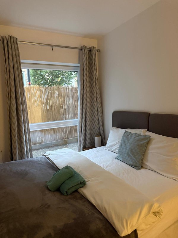 Bright bedroom with double bed, green pillows, patio doors and garden view
