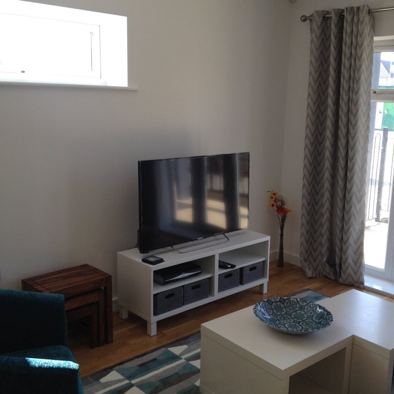Living room with TV on white stand, wooden floor, patterned curtains and glass door