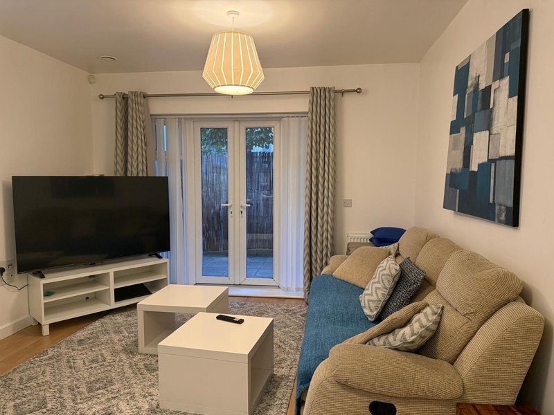 Modern living room with beige sofa, TV, white coffee table and glass doors to garden