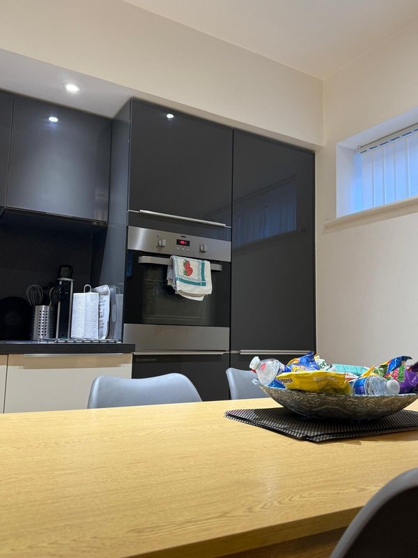 Modern kitchen with yellow dining table, black cabinetry, built-in oven, and fruit bowl
