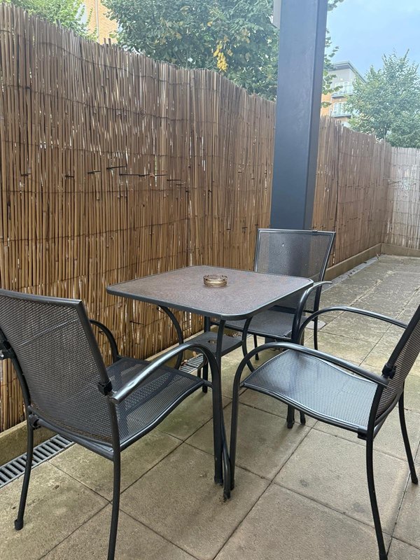 Outdoor patio area with dining table, chairs, wooden fence and large pillar