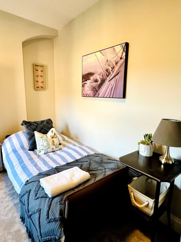 Small bedroom with single bed, blue striped bedding, wooden nightstand, wall art and potted plant
