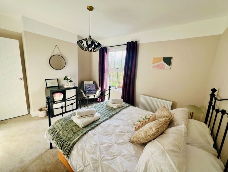 Bright bedroom with double bed, black metal frame, dresser, round mirror and purple curtains