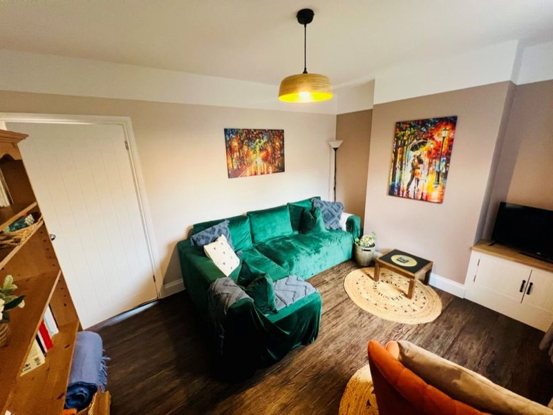 Living room with teal sofa, wooden furniture, colorful wall art, and pendant lamp
