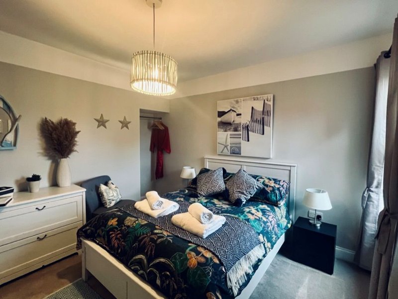Bedroom with double bed, patterned bedding, pendant light, dresser and wall decor