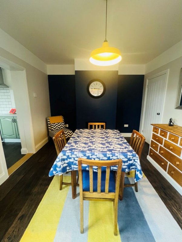 Dining room with wooden table, chairs, blue tablecloth, pendant light and black accent wall