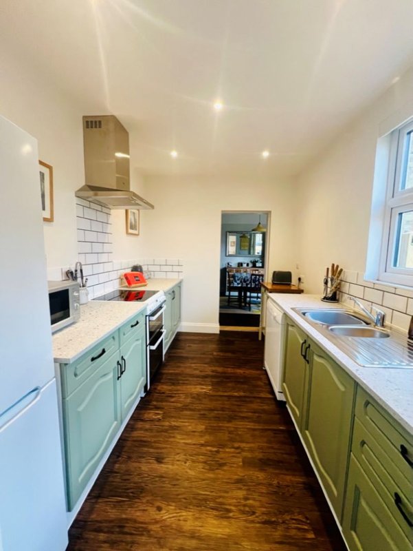 Galley kitchen with pale green cabinetry, white subway tile backsplash, and wooden flooring