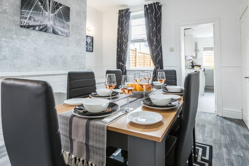 Modern dining room with wooden table, black chairs, place settings and window with curtains
