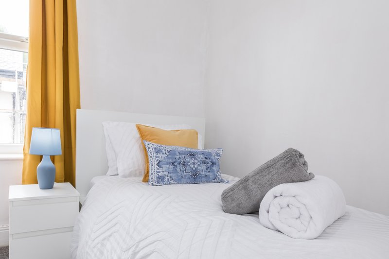 Bright bedroom with white bed, yellow curtains, blue patterned pillow and gray cushion