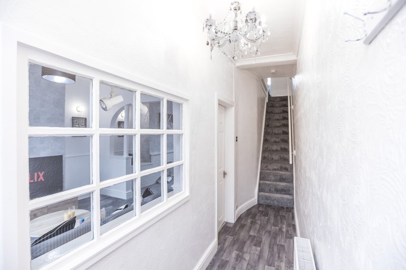 Bright hallway with white walls, wooden flooring, crystal chandelier, and staircase visible ahead