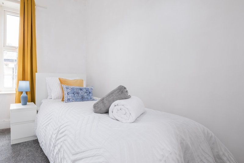 Bright bedroom with white double bed, grey carpet, yellow curtains and window
