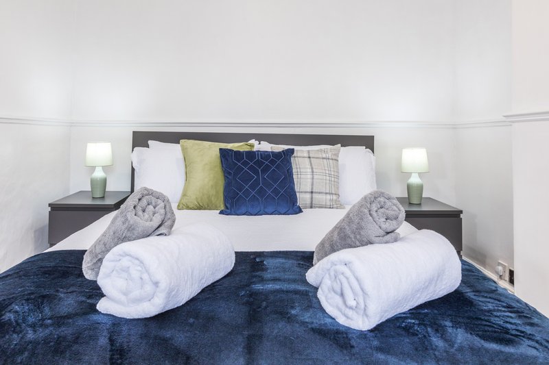 Bedroom with double bed, grey headboard, rolled towels, decorative pillows and bedside lamps