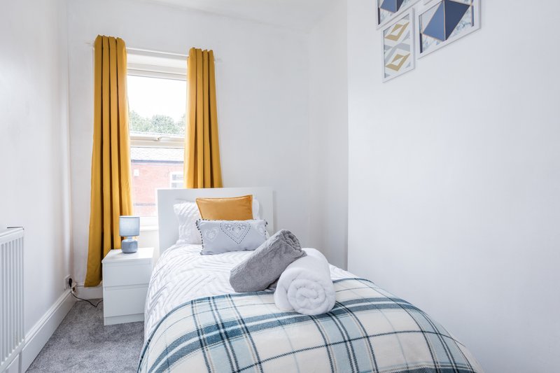 Bright bedroom with single bed, yellow curtains, white bedside table and window view