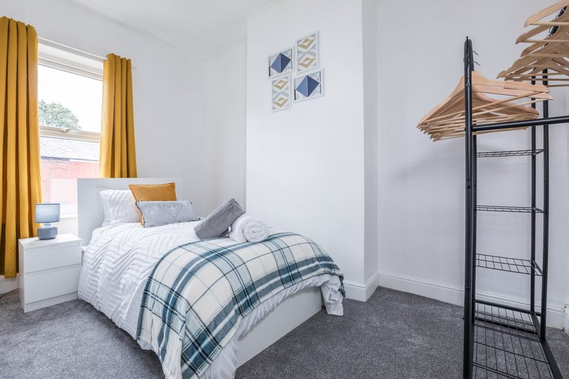 Bright bedroom with single bed, yellow curtains, white walls and grey carpet flooring