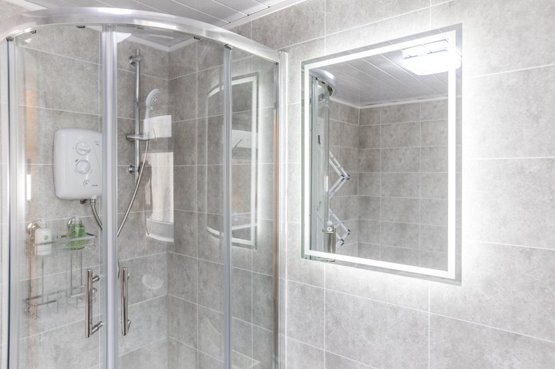 Modern bathroom with walk-in shower, illuminated mirror and grey tile walls