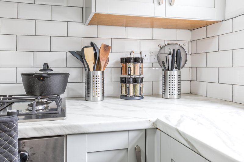 Clean white kitchen with subway tiles, stainless steel utensil holders, cookware and marble countertop