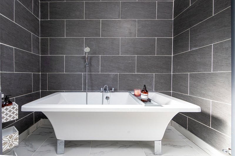 Modern bathroom with freestanding white bathtub, grey tile walls, and chrome fixtures