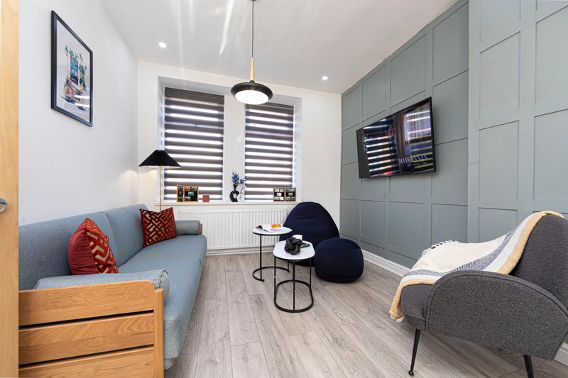 Modern living room with blue sofa, grey armchair, pendant lighting and wall-mounted screens