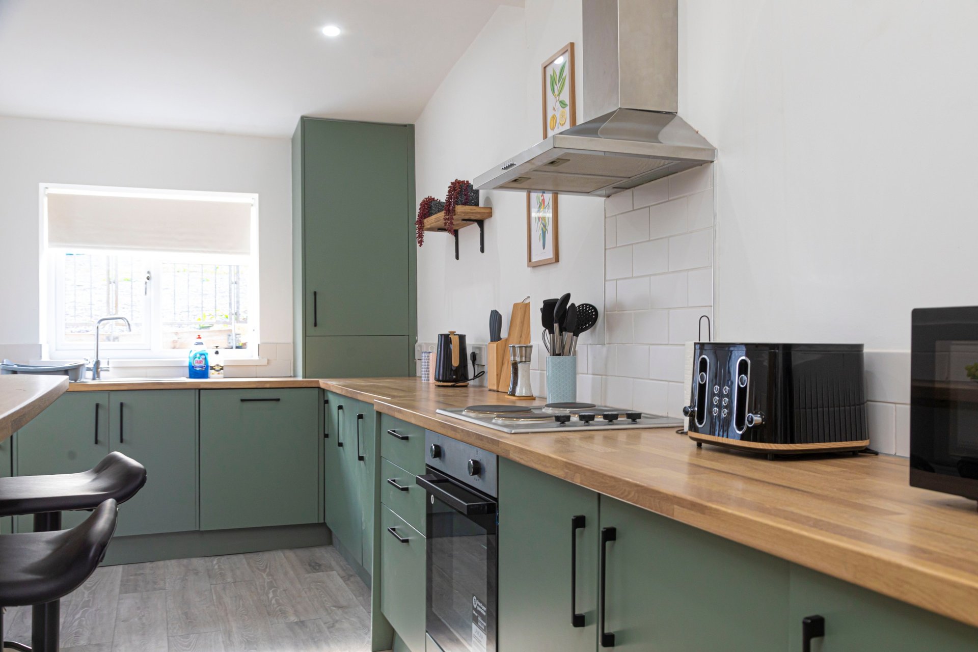Modern kitchen with green cabinetry, wooden countertop, stainless steel range hood and appliances