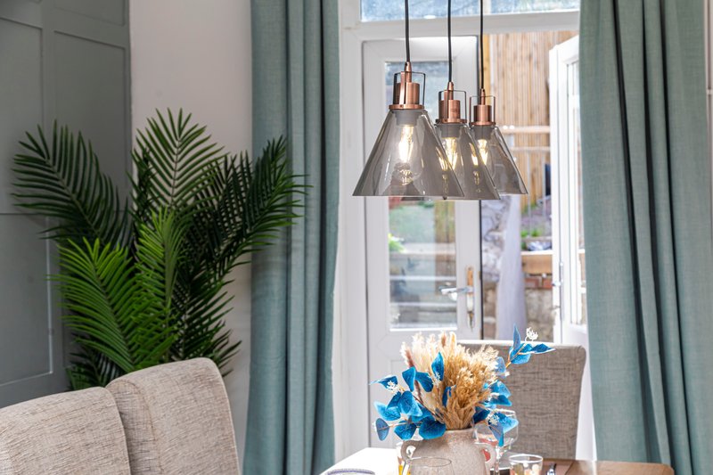 Dining area with potted plant, pendant lights, blue flowers, and garden view through window