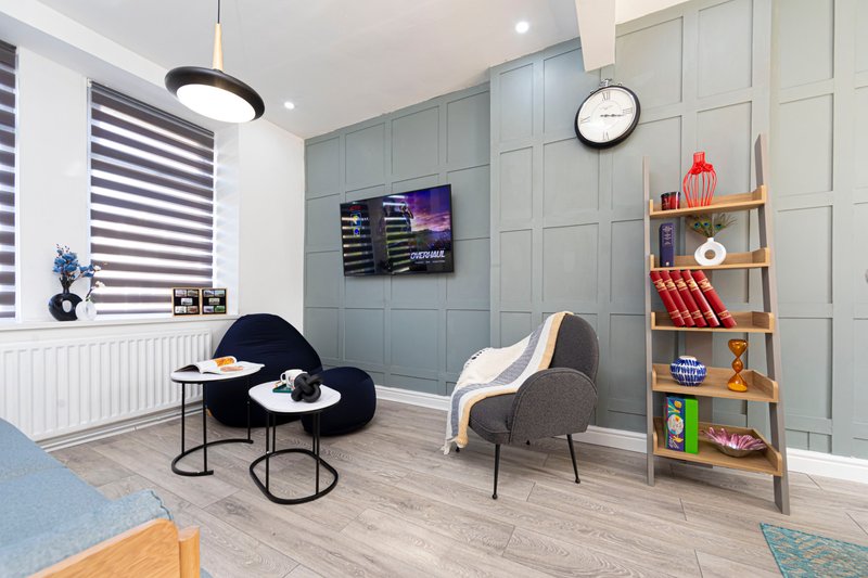 Modern living room with black curved chair, wooden shelving, wall-mounted TV, and gray paneling