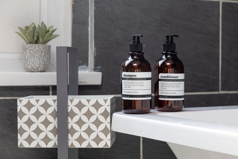 Modern bathroom counter with shampoo and conditioner bottles, potted plant, and geometric tissue box