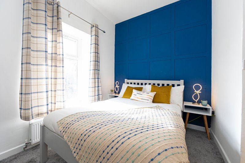 Bedroom with double bed, blue feature wall, patterned bedding and plaid curtains