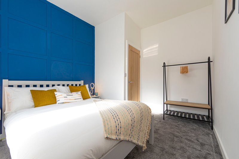 Modern bedroom with double bed, blue headboard, yellow pillows, and clothing rack