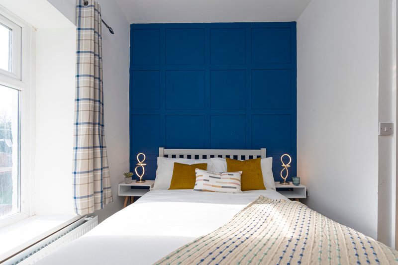 Modern bedroom with double bed, blue padded headboard, mustard cushions and bedside lamps
