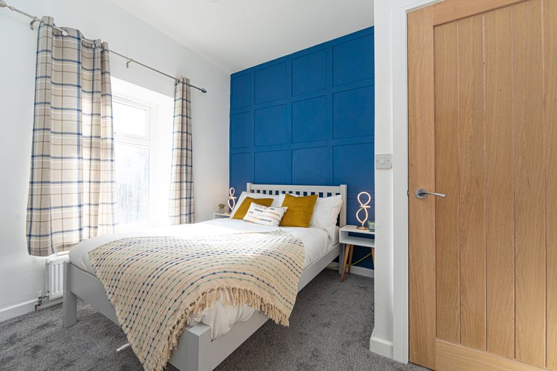 Modern bedroom with double bed, blue feature wall, patterned curtains and wooden door