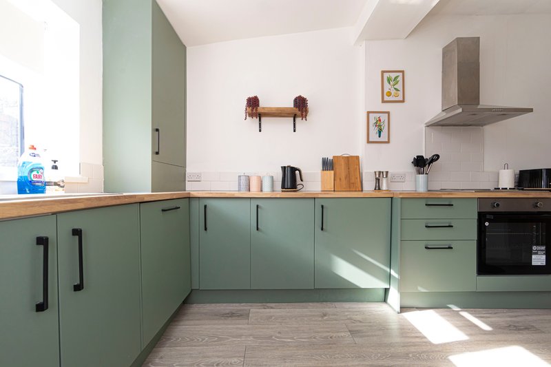 Modern kitchen with sage-green cabinetry, wooden countertop, stainless steel range hood and black oven