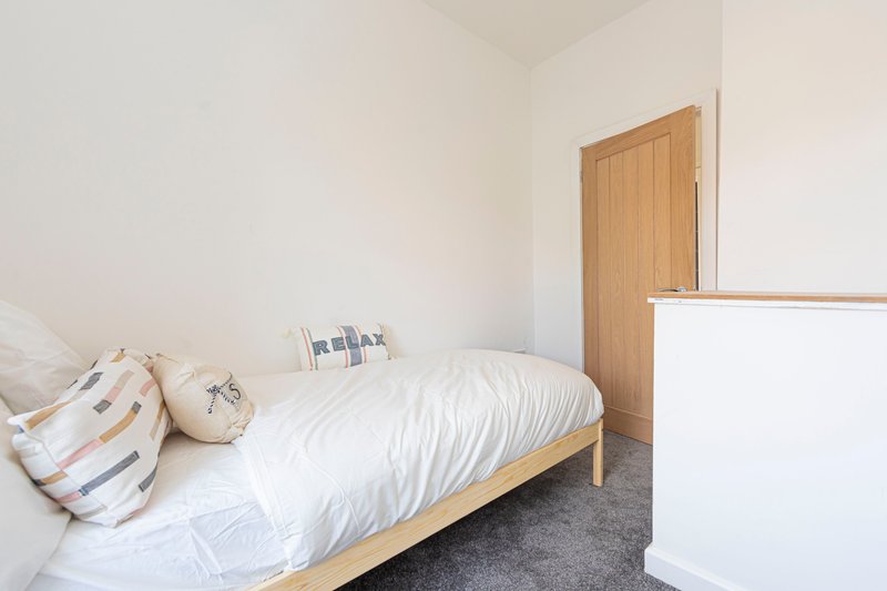 Bright bedroom with single bed, wooden frame, white bedding and decorative pillows
