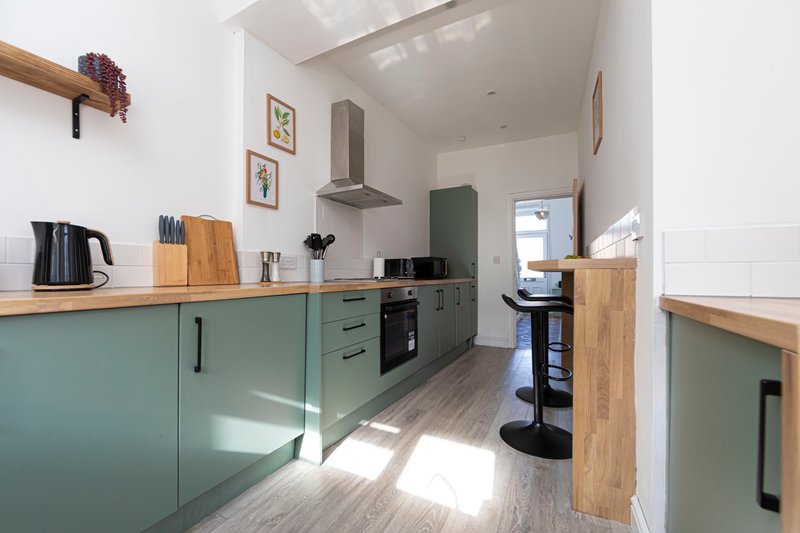 Modern kitchen with green cabinetry, wooden worktops, black appliances and bar seating