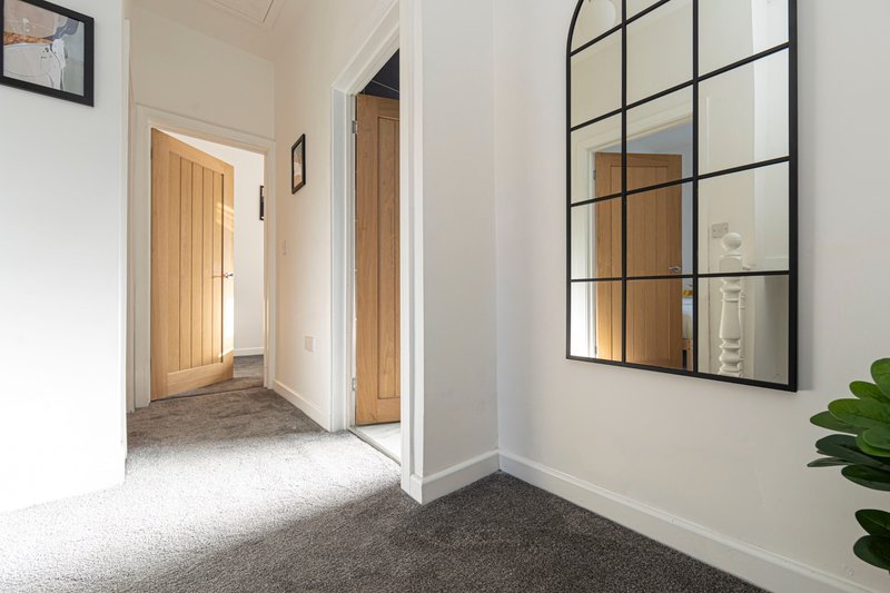 Bright hallway with white walls, wooden doors, grid-pattern mirror and potted plant