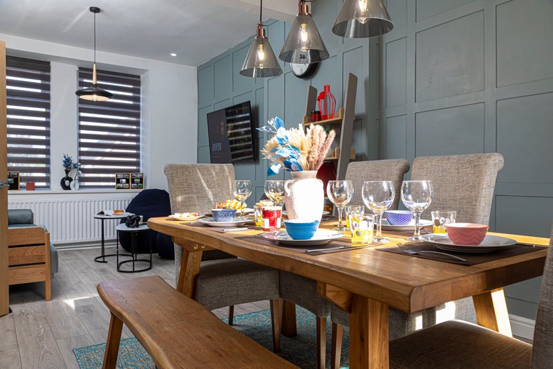 Modern dining room with wooden table, upholstered chairs, pendant lights and open-plan kitchen