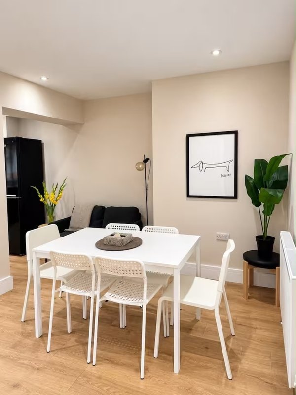 Modern dining room with white table, four chairs, framed wall art, and potted plant