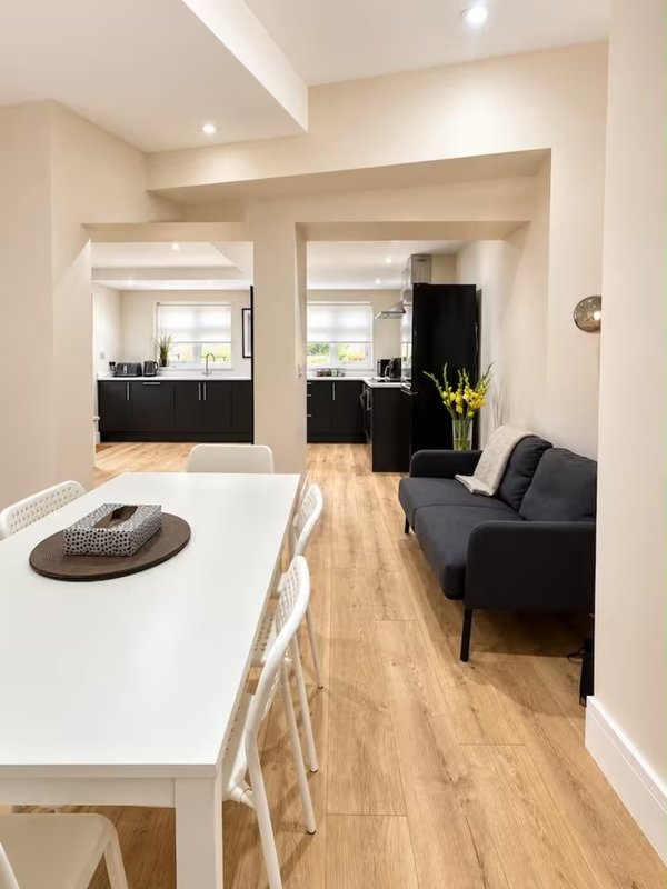 Open-plan kitchen and living area with white dining table, black sofa, and wooden flooring throughout