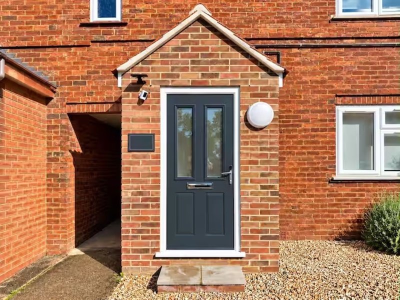 Red brick house exterior with dark blue door, small porch, and gravel driveway