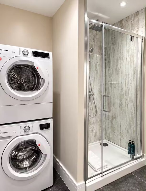Laundry room with stacked white washing machines and glass-enclosed shower enclosure
