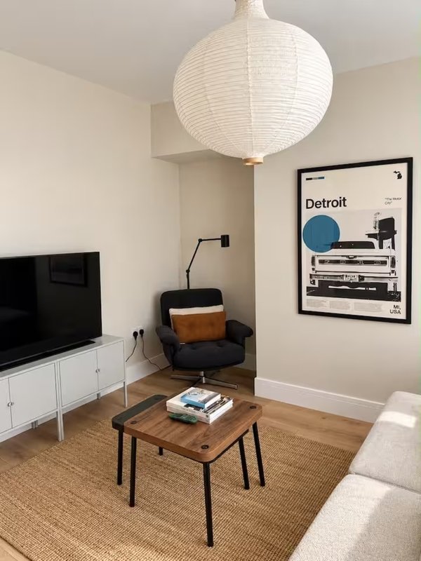 Living room with wooden table, black chair, white pendant lamp, TV, and framed Detroit poster