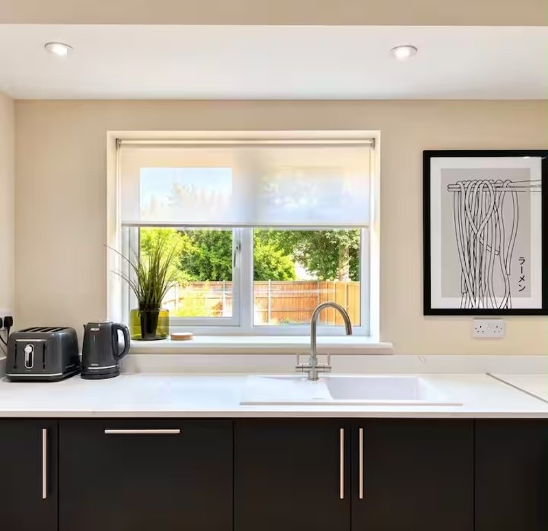 Modern kitchen with black cabinetry, white countertop, sink and window overlooking garden