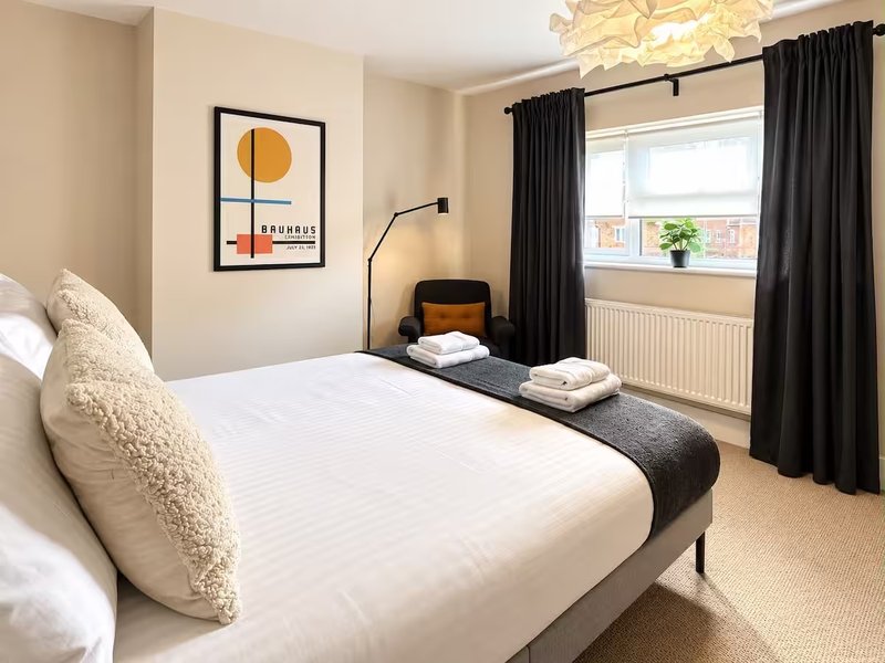 Bright modern bedroom with double bed, cream bedding, black curtains and abstract wall art